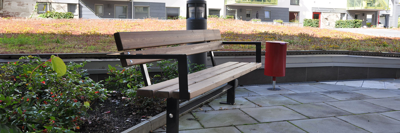 Un banc de parc avec dossier et une poubelle à côté, le long d'une allée.